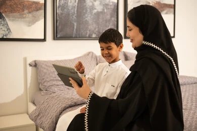 أم سعودية وابنها يستخدمان الجهاز اللوحي في غرفة النوم أم سعودية وابنها يستخدمان الجهاز اللوحي في غرفة النوم