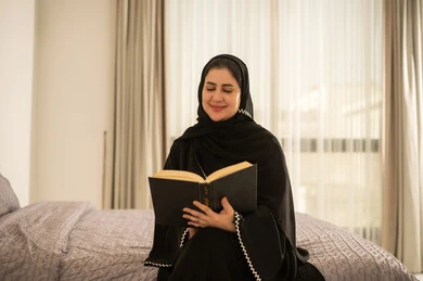 امرأة سعودية تقرأ كتاب في غرفة نوم مضيئة