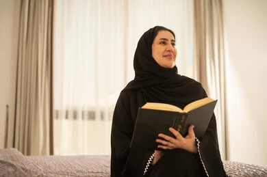 امرأة سعودية بالعباءة تقرأ كتاباً في المنزل