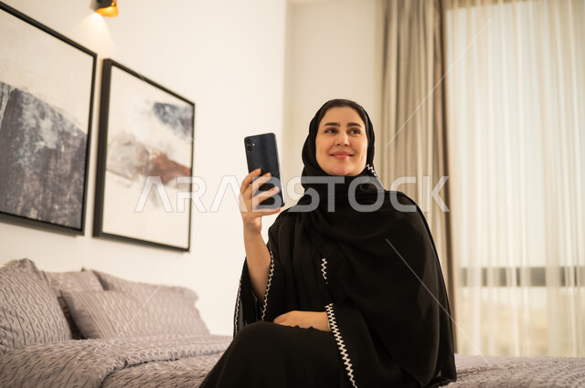 امرأة سعودية بالعباءة تستخدم الهاتف الذكي في غرفة النوم