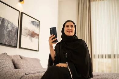 امرأة سعودية بالعباءة تستخدم الهاتف الذكي في غرفة النوم