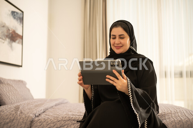 امرأة سعودية بالعباءة تستخدم جهاز لوحي في غرفة النوم