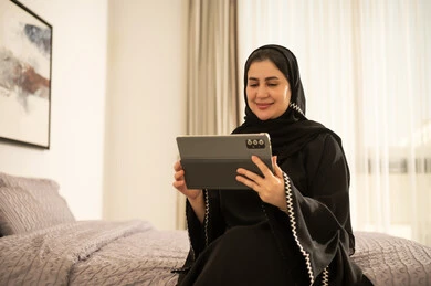 امرأة سعودية بالعباءة تستخدم جهاز لوحي في غرفة النوم