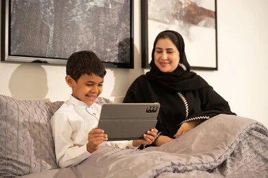 امرأة وطفل سعودي يستخدمان جهازاً لوحياً في غرفة نوم