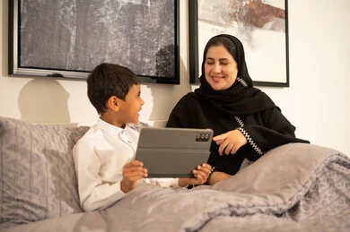 امرأة سعودية وطفل يستخدمان الجهاز اللوحي في السرير