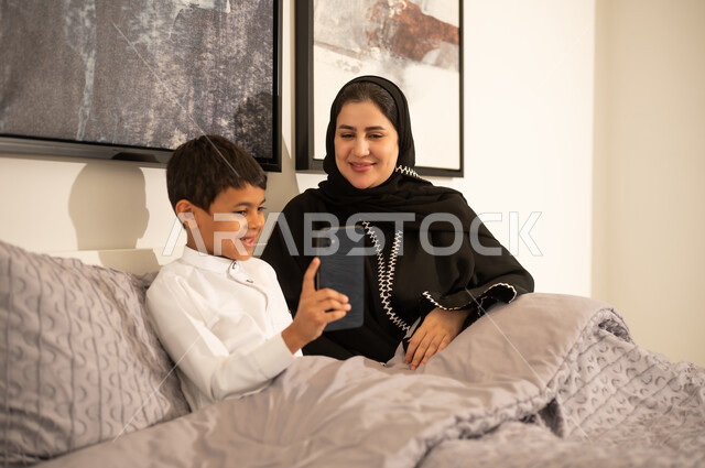 أم سعودية وابنها يستخدمان الهاتف الذكي في السرير
