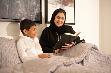 أم سعودية تقرأ كتاباً لابنها الصغير في غرفة النوم