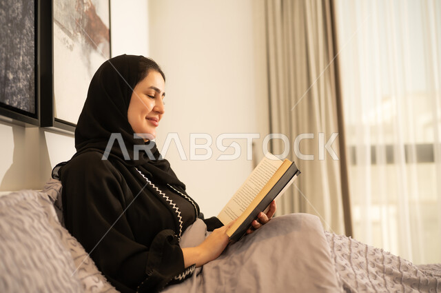 امرأة سعودية تقرأ كتاباً في غرفة النوم بإضاءة طبيعية