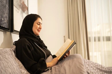 امرأة سعودية تقرأ كتاباً في غرفة النوم بإضاءة طبيعية