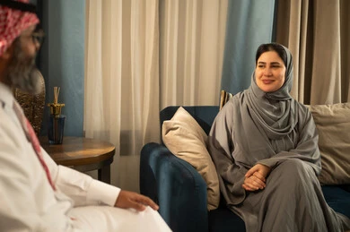 امرأة سعودية بعباءة رمادية تبتسم أثناء حديث عائلي