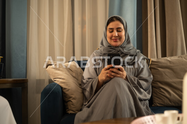 امرأة سعودية بعباءة رمادية تستخدم الهاتف في المنزل