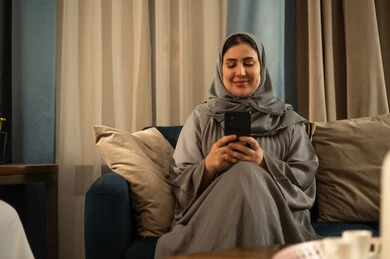 امرأة سعودية بعباءة رمادية تستخدم الهاتف في المنزل