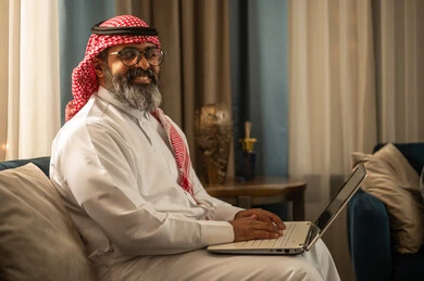 رجل سعودي يستخدم اللابتوب باللباس التقليدي في المنزل