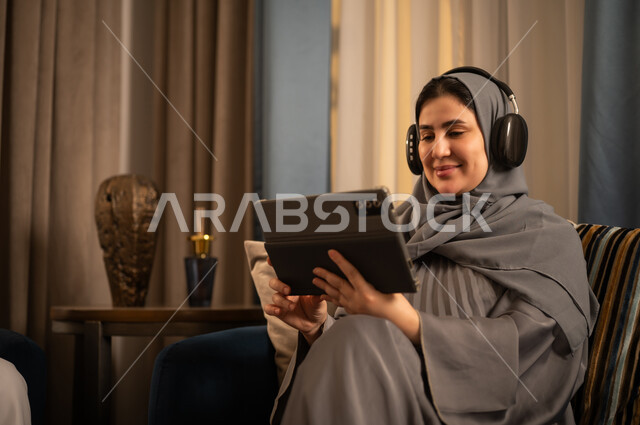 امرأة سعودية تستخدم جهاز لوحي مع سماعات في المنزل