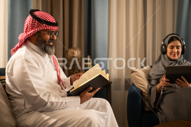 رجل سعودي يقرأ كتاباً وامرأة تستخدم جهازاً لوحياً