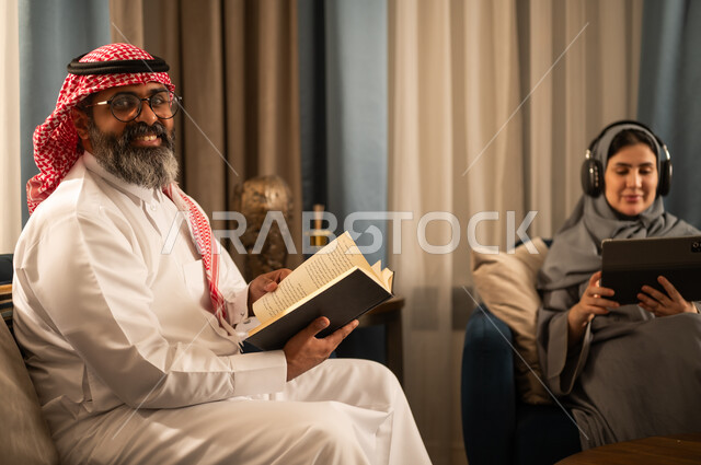 رجل سعودي يقرأ كتاباً مع امرأة تستخدم جهازاً لوحياً