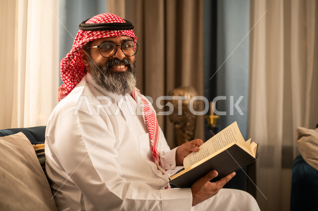رجل سعودي باللباس التقليدي يقرأ كتاباً في المنزل