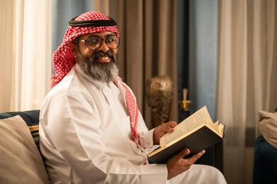 Saudi Man in Traditional Dress Reading Book Indoors