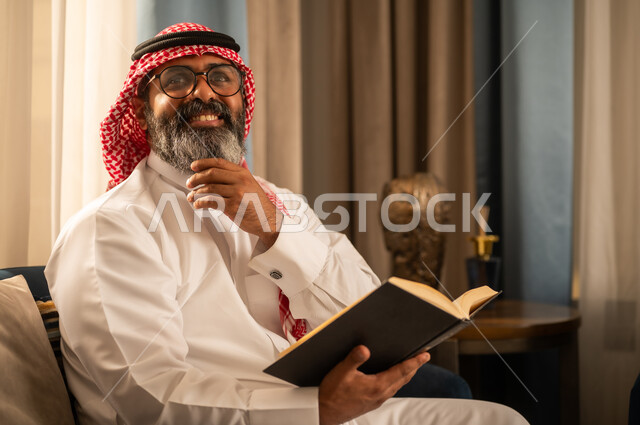رجل سعودي باللباس التقليدي يقرأ كتاباً في المنزل
