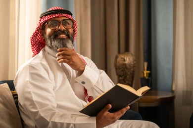 رجل سعودي باللباس التقليدي يقرأ كتاباً في المنزل