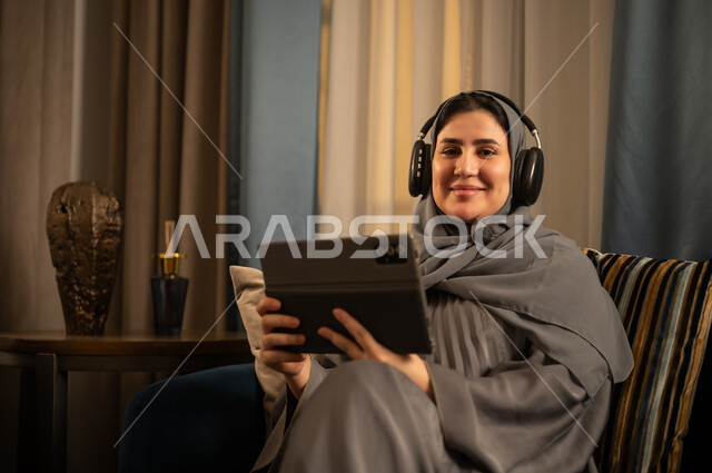 امرأة سعودية تستخدم جهازاً لوحياً وسماعات في المنزل
