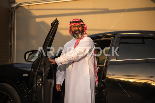 رجل سعودي بالزي التقليدي بجانب سيارة فاخرة