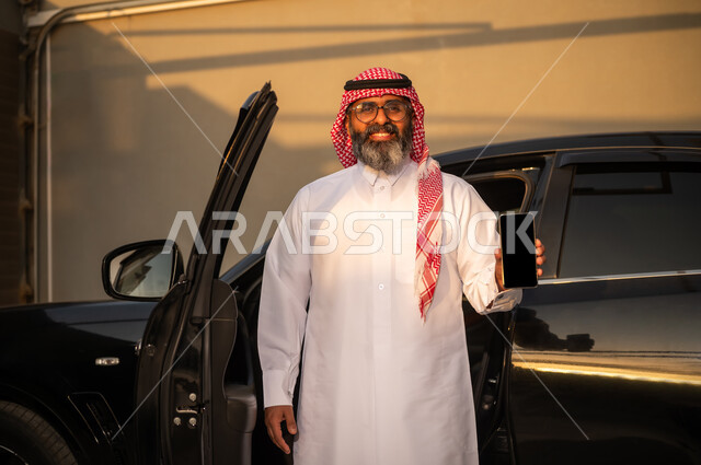 رجل سعودي يمسك هاتف بجانب سيارة وقت الغروب