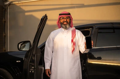 رجل سعودي يمسك هاتف بجانب سيارة وقت الغروب