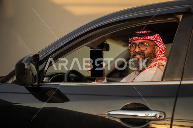 رجل سعودي في السيارة يحمل هاتفاً ذكياً بشاشة فارغة