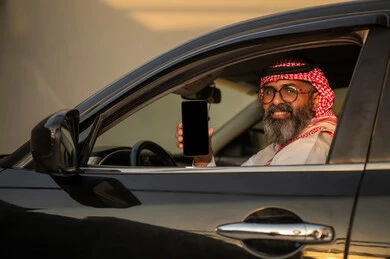 رجل سعودي في السيارة يحمل هاتفاً ذكياً بشاشة فارغة
