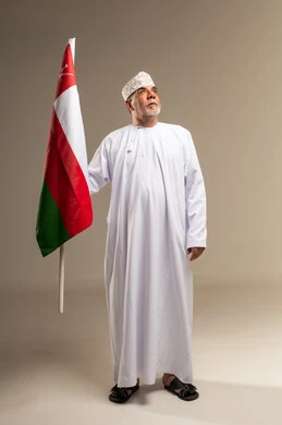 رجل عماني يرفع العلم بالزي العماني التقليدي