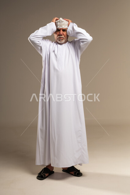 رجل عماني مسن بالزي التقليدي يضع يديه على رأسه