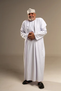 رجل عماني مسن يرتدي الدشداشة والكمة التقليدية مبتسماً