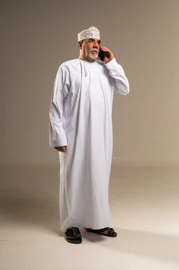 رجل عُماني مسن بالزي التقليدي يستخدم الهاتف الذكي