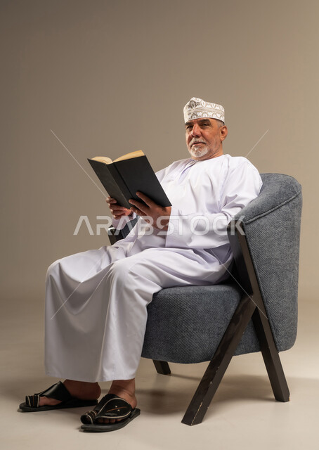 Elderly Omani Man in Traditional Dress Reading a Book