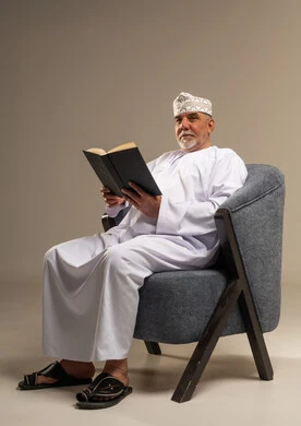 رجل عماني مسن بالزي التقليدي يقرأ كتابا في استوديو