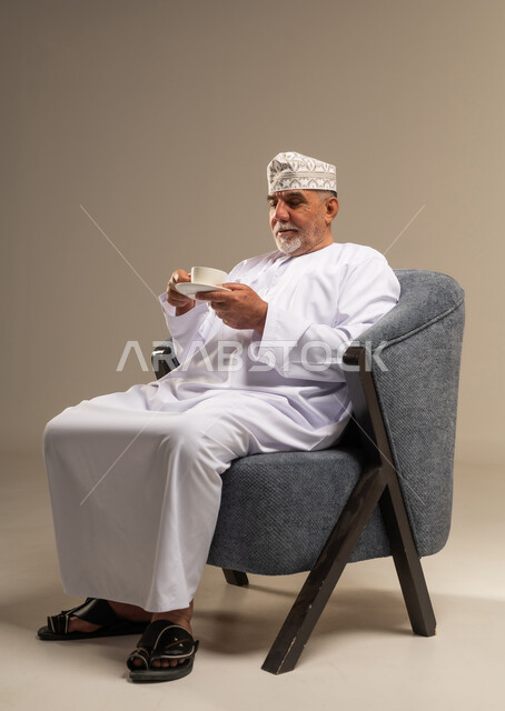 Senior Omani Man Sitting in Armchair Drinking Tea in Studio