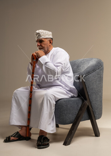 رجل عُماني مسن يمسك عكازاً على مقعد مريح