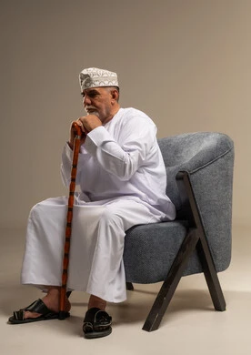 رجل عُماني مسن يمسك عكازاً على مقعد مريح