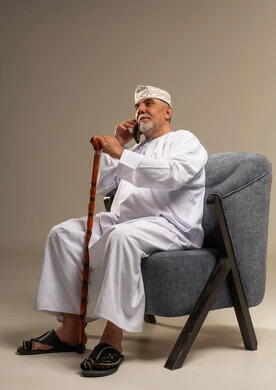 رجل عُماني مسن يتحدث بالهاتف جالسًا على كرسي