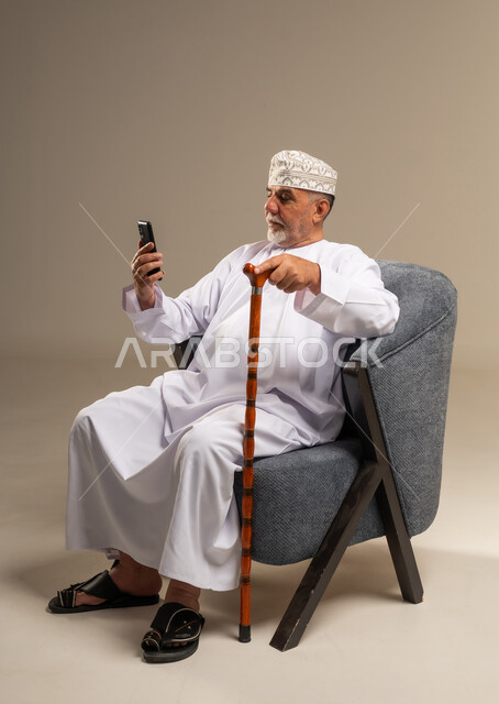 Elderly Omani Man Using Smartphone in Armchair