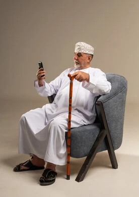 Elderly Omani Man Using Smartphone in Armchair