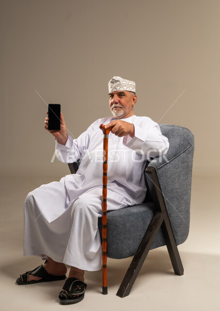 رجل عُماني مسن يحمل هاتف ذكي وعصا مشي