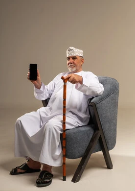 رجل عُماني مسن يحمل هاتف ذكي وعصا مشي
