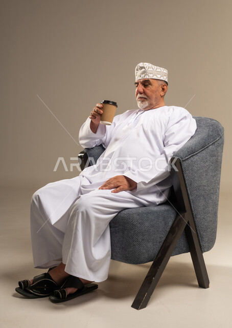 رجل عماني كبير في السن بالزي التقليدي يحمل كوب قهوة