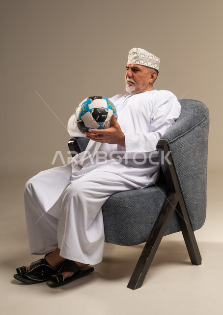 رجل عُماني مسن بالزي التقليدي يمسك كرة قدم