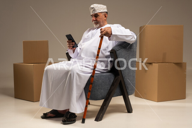 Senior Omani Man Using Smartphone with Delivery Boxes