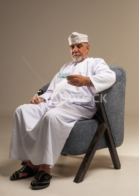 رجل عماني مسن بالزي التقليدي يمسك نقوداً
