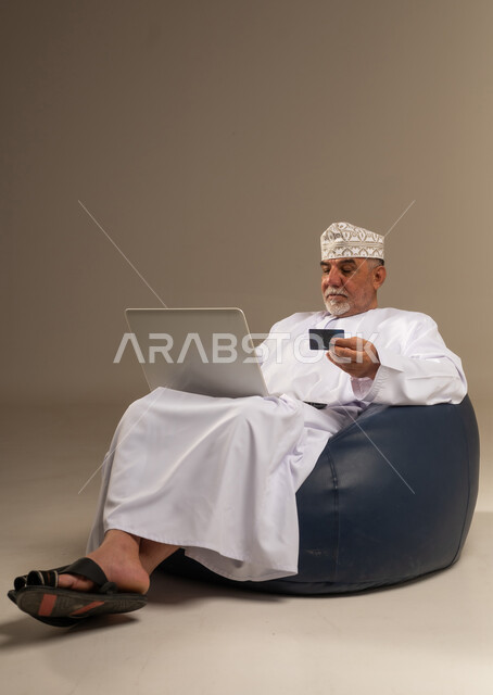 رجل عُماني مسن يستخدم المحمول وبطاقة الائتمان