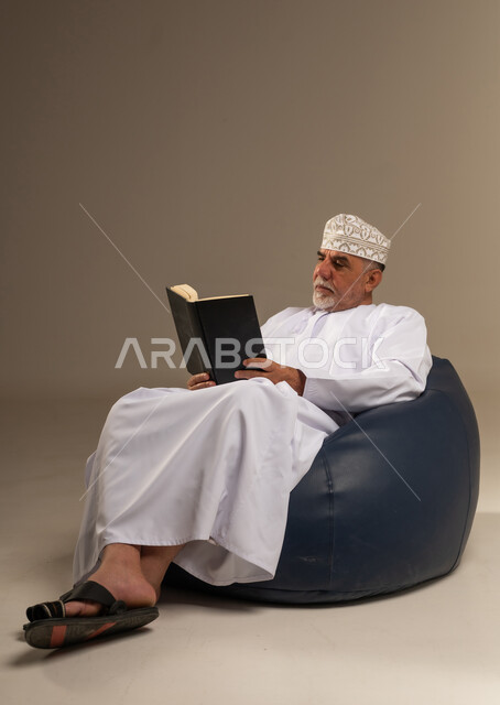 Elderly Omani Man Reading Book in Traditional Attire